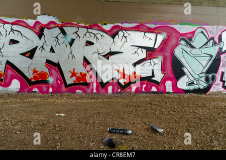 Graffiti su un muro sotto un ponte con la vernice spray teglie lasciato sul terreno, Nottingham, Inghilterra, Regno Unito Foto Stock