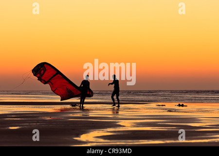 Sagome di due uomini a piedi sulla spiaggia con un kite surfer vela al tramonto, Essaouira, Marocco, Africa Foto Stock