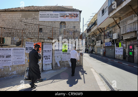 Banner in alto su una casa con norme di comportamento per i turisti, a parete quotidiani e un ebreo ortodosso con un telefono cellulare nella parte anteriore in Foto Stock