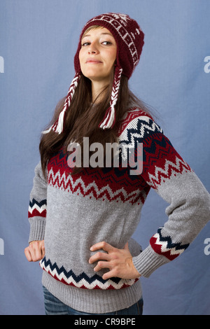 Giovane e bella donna che indossa un pullover e cappello di lana in posa con le mani sui fianchi. Funny studio shot contro un fondo azzurro Foto Stock