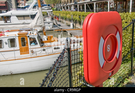 Rosso brillante alloggiamento in plastica per un salvagente a St Katherine's Dock a Londra con imbarcazioni da diporto ormeggiata in modo sicuro nella marina. Foto Stock