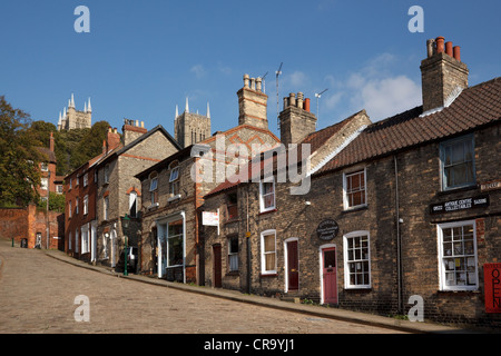 Il vecchio tradizionale negozio terrazzati fronti e case sulla strada di ciottoli, ripida collina, Lincoln, Lincolnshire, England, Regno Unito Foto Stock