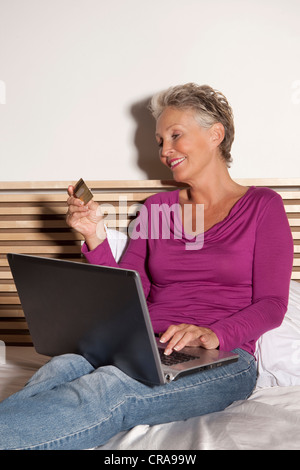 Donna anziana lo shopping online su letto Foto Stock