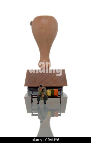 Figura in miniatura di una persona senza dimora seduta su una panchina di fronte a un timbro, immagine simbolica di essere etichettati Foto Stock