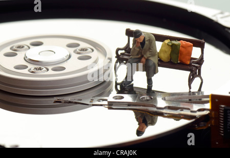 Figura in miniatura di una persona senza dimora seduta su una panchina su un disco rigido, immagine simbolica per dati ingombra Foto Stock