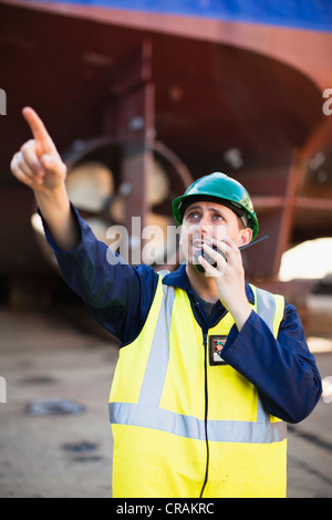 Lavoratore utilizzando walkie talkie sul bacino di carenaggio Foto Stock