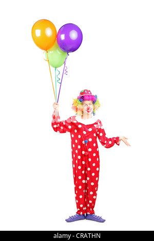 A piena lunghezza verticale di una femmina di clown, felice espressione gioiosa sul volto, con un mucchio di palloncini isolati su sfondo bianco Foto Stock