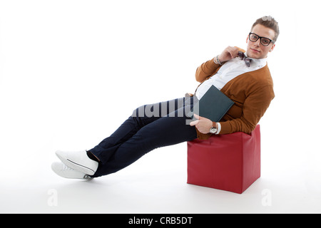 Giovane uomo con gli occhiali e un filtro bow tie seduto su un cubo Foto Stock