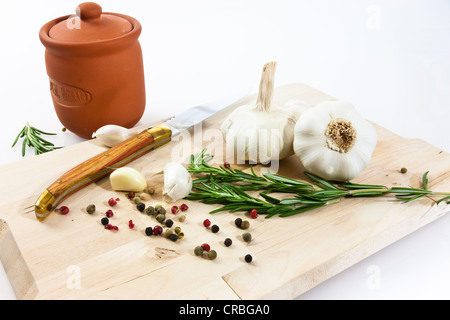 L'aglio (allium sativum) su una tavola di legno con coltello, pentola di creta, rosmarino e in bianco e nero e il pepe rosso Foto Stock