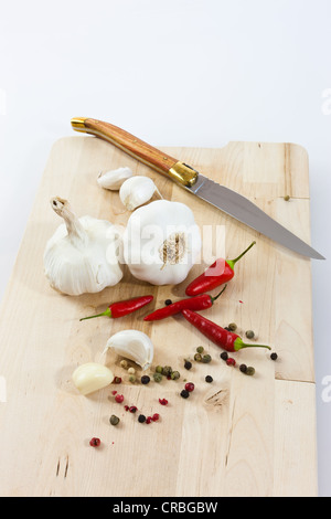 L'aglio (allium sativum) su una tavola di legno con coltello, chilis e in bianco e nero e il pepe rosso Foto Stock