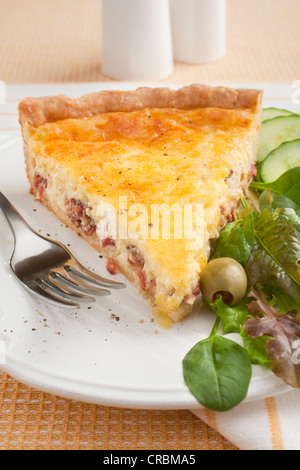 Una fetta di quiche lorraine o uova e pancetta flan, su una piastra con insalata. Foto Stock