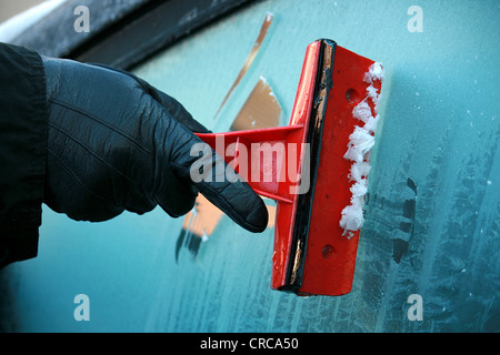 Nero a mano utilizzando un ghiaccio rosso raschiatore su un effetto smerigliato finestra auto Foto Stock