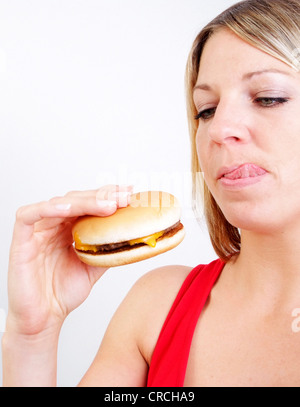 Giovane donna bionda con burger, leccare le sue labbra Foto Stock