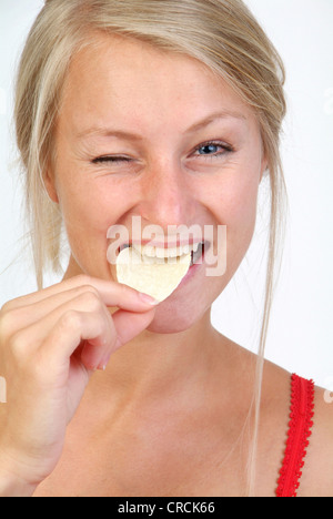 Giovane donna bionda che mangia patatine, strizzare gli occhi in un occhio Foto Stock