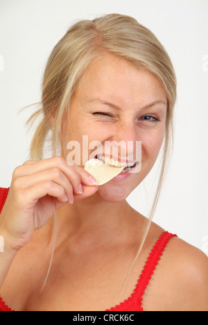 Giovane donna bionda che mangia patatine, strizzare gli occhi in un occhio Foto Stock