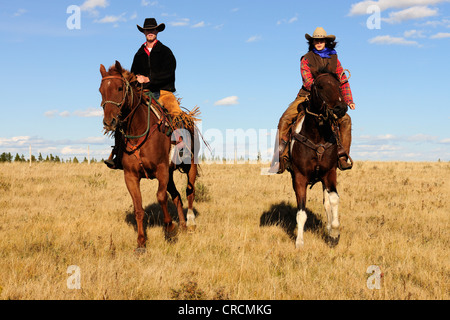 Un cowgirl e un cowboy a cavallo attraverso la prairie, Saskatchewan, Canada Foto Stock