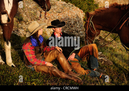 Cowgirl e cowboy seduto per terra tenendo i loro cavalli da le redini, Saskatchewan, Canada, America del Nord Foto Stock