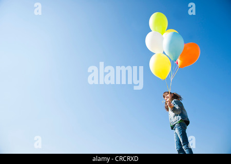 Ragazza in piedi con palloni sotto il cielo blu Foto Stock