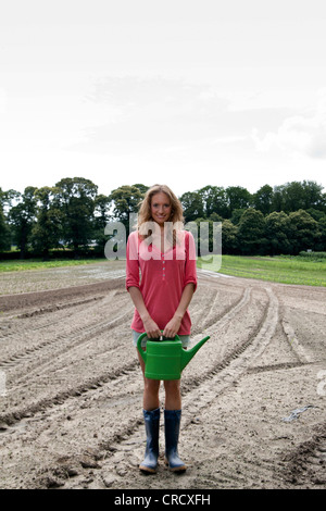 Giovane donna con annaffiatoio sul campo Foto Stock