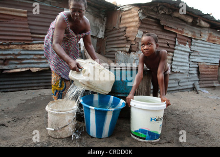 Una ragazza orologi mentre una donna che preleva acqua da un pozzo in un punto ad ovest delle baraccopoli a Monrovia, Montserrado county, Liberia Foto Stock