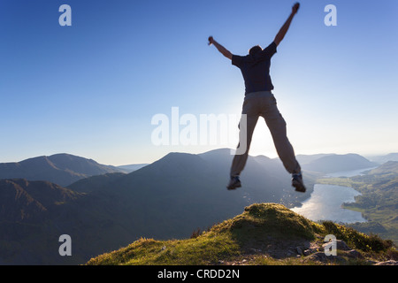 L'uomo celebrando, saltare in aria con braccia tese sulla cima di una montagna. Foto Stock