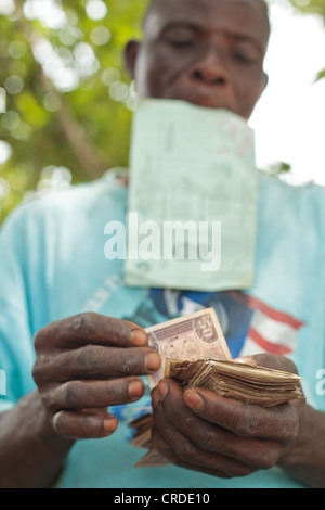 Un uomo conta i soldi che ha appena ricevuto da una cassa sociale programma di trasferimento nel villaggio di Julijuah, Liberia Foto Stock