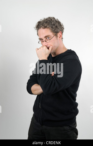 Giovane Uomo con occhiali tenendo la sua mano sulla sua bocca, con le braccia incrociate, cercando scettico Foto Stock