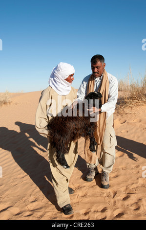 Bedouin tenendo un giovane capra nelle sue braccia, dune di sabbia del deserto del Sahara tra Douz e Ksar Ghilane, Tunisia meridionale, Tunisia Foto Stock