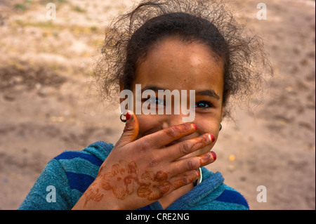 Ritratto, sorridente ragazza con la sua mano decorata con motivi henna davanti la sua bocca Skoura, Marocco, Africa Foto Stock