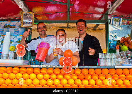 Tre ridere gli uomini offrendo spremuta di arancia al loro stand, Djemaa el Fna, quadrato dell'impiccato, Marrakech, Marocco Foto Stock