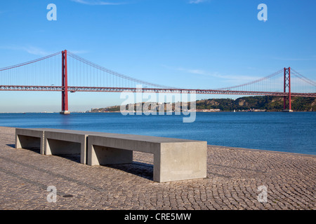 Panca sulla riva del Rio Tejo fiume nella parte anteriore del Ponte do 25 de Abril bridge nel quartiere di Belem, Lisbona, Portogallo Foto Stock