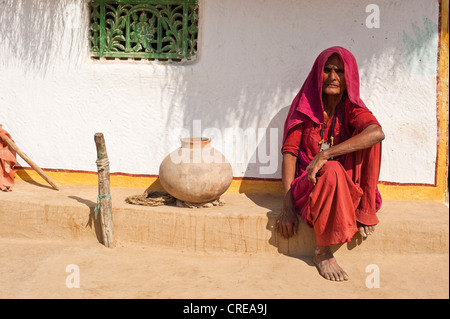 Una donna indiana in un sari rosso seduto accanto a un'argilla boccale acqua di fronte alla sua casa, nel deserto di Thar, Rajasthan, India, Asia Foto Stock