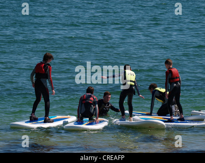 I bambini ad imparare a stare su un stand up paddle-board, Swanpool, Falmouth, Cornwall, Regno Unito Foto Stock