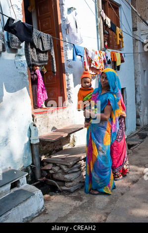 Gentile giovane donna indiana indossando un sari trasporta un bambino piccolo sul suo braccio è in piedi di fronte ad una porta, Udaipur Foto Stock