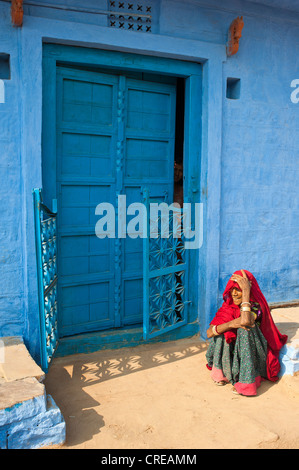 Anziani donna indiana seduta sul pavimento nella parte anteriore del suo blu-casa dipinta, Bishnoi, Jodhpur, Rajasthan, India, Asia Foto Stock