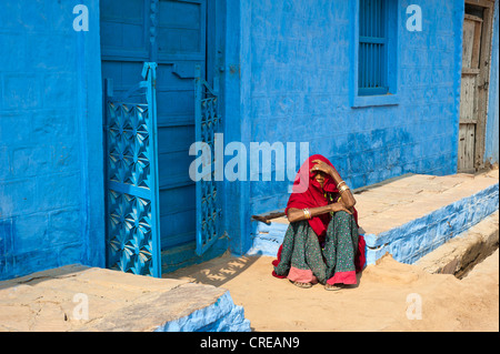 Anziani donna indiana seduta sul pavimento nella parte anteriore del suo blu-casa dipinta, Bishnoi, Jodhpur, Rajasthan, India, Asia Foto Stock