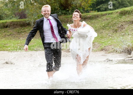 Sposa in abito da sposa e lo sposo in abito nuziale in esecuzione nel fiume Danubio, Regensburg, Baviera, Germania, Europa Foto Stock