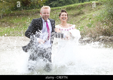 Sposa in abito da sposa e lo sposo in abito nuziale in esecuzione nel fiume Danubio, Regensburg, Baviera, Germania, Europa Foto Stock