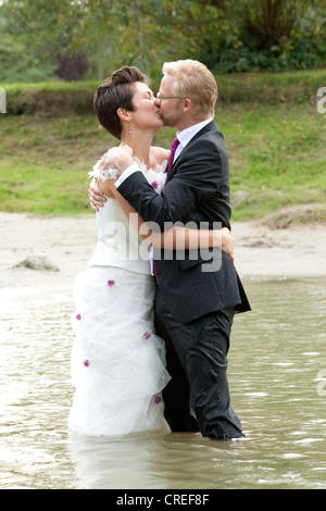 Sposa in abito da sposa e lo sposo in abito nuziale baciare in fiume Danubio in Regensburg, Baviera, Germania, Europa Foto Stock