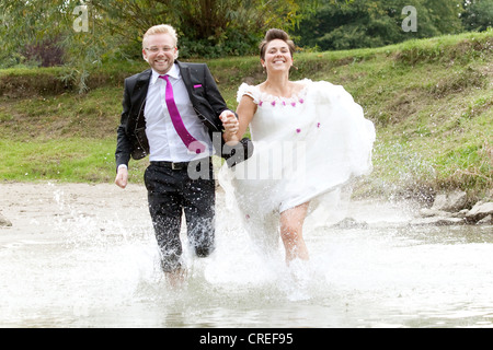 Sposa in abito da sposa e lo sposo in abito nuziale in esecuzione nel fiume Danubio, Regensburg, Baviera, Germania, Europa Foto Stock