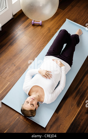 Donna incinta a praticare yoga sul tappetino Foto Stock