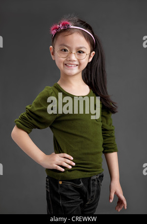 Felice 5 anni cinese ragazza sorridente ,indossa occhiali,mano permanente sull'anca. Foto Stock