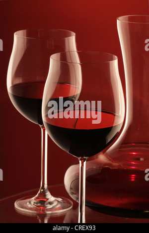 Due bicchieri di vino rosso e il decanter su sfondo rosso Foto Stock