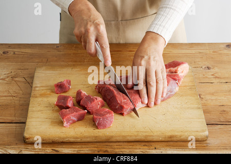 La donna il taglio di carne a fette sulla tavola di legno Foto Stock