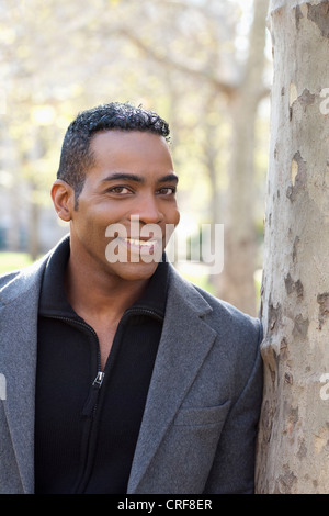 Ritratto di sorridere African American uomo appoggiato contro il tronco di albero Foto Stock