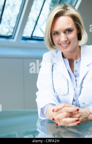 Medico sorridente seduto alla scrivania Foto Stock