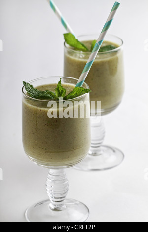 Verde frullati di frutta con kiwi, verde uva e menta, con un tocco di miele, in vetro chiaro con verde/bianco striato cannucce. Foto Stock