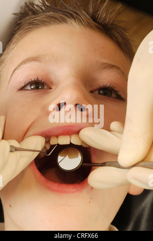 Un dentista utilizza un dentista di prelevamento e specchio dentale per esaminare le condizioni di un giovane maschio i denti e le gengive. Foto Stock