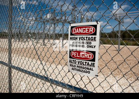 Alta tensione di segno di pericolo sulla catena collegamento recinto a energia solare farm in Texas in inglese e spagnolo Foto Stock
