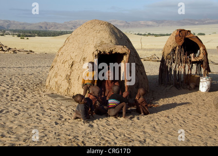 Il villaggio tradizionale di Purros, Himba donna con i bambini di fronte a una capanna, Namibia, Purros Foto Stock